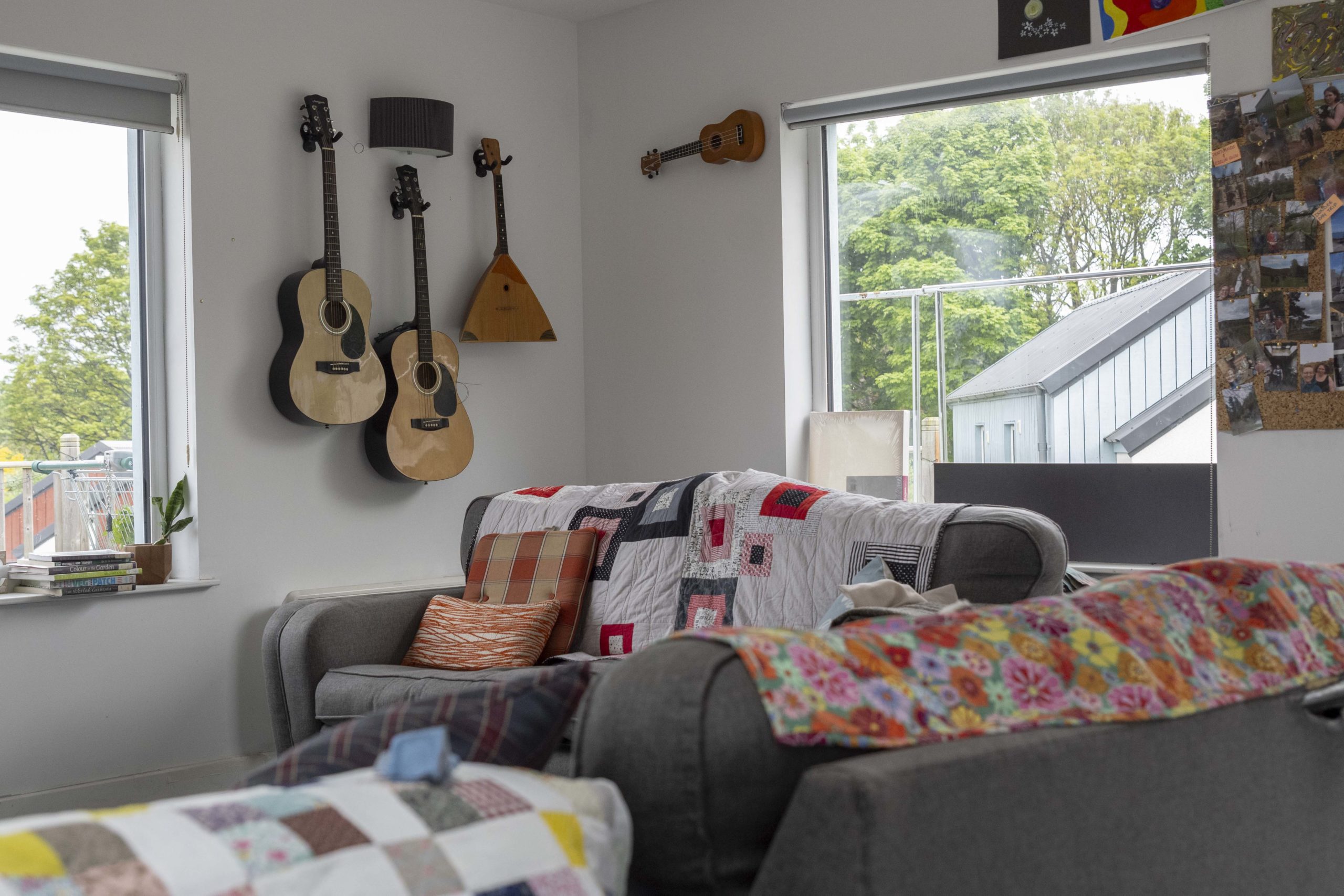 A living room with grey sofas covered in bright blankets and guitars hanging on the wall