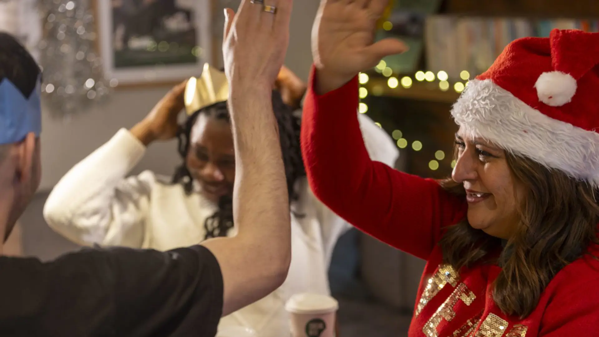 A woman in a Santa hat and a red jumper high-fives a man in a black tshirt